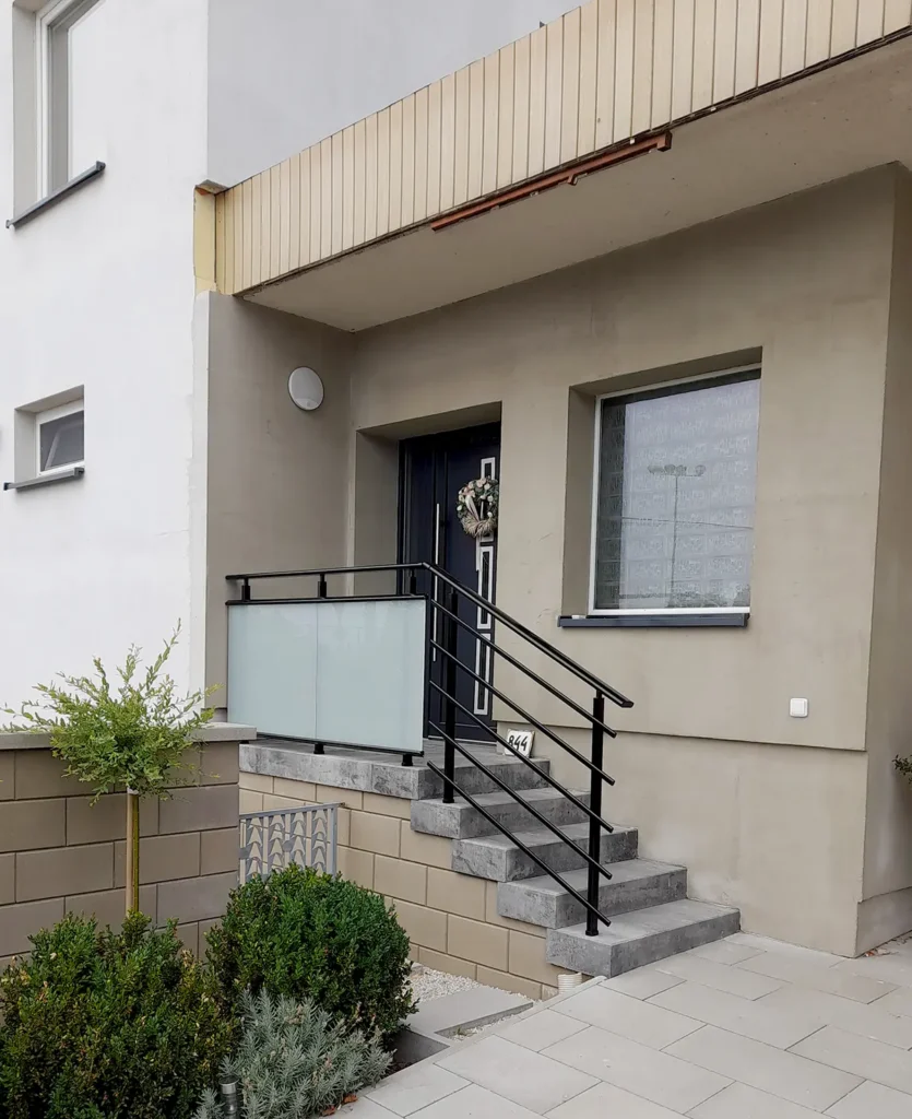 Černé kovové zábradlí s mléčným sklem u vchodu do rodinného domu.