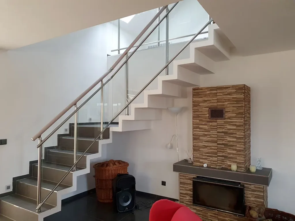 Nerezové zábradlí se skleněnou výplní na vnitřním schodišti v moderním interiéru.