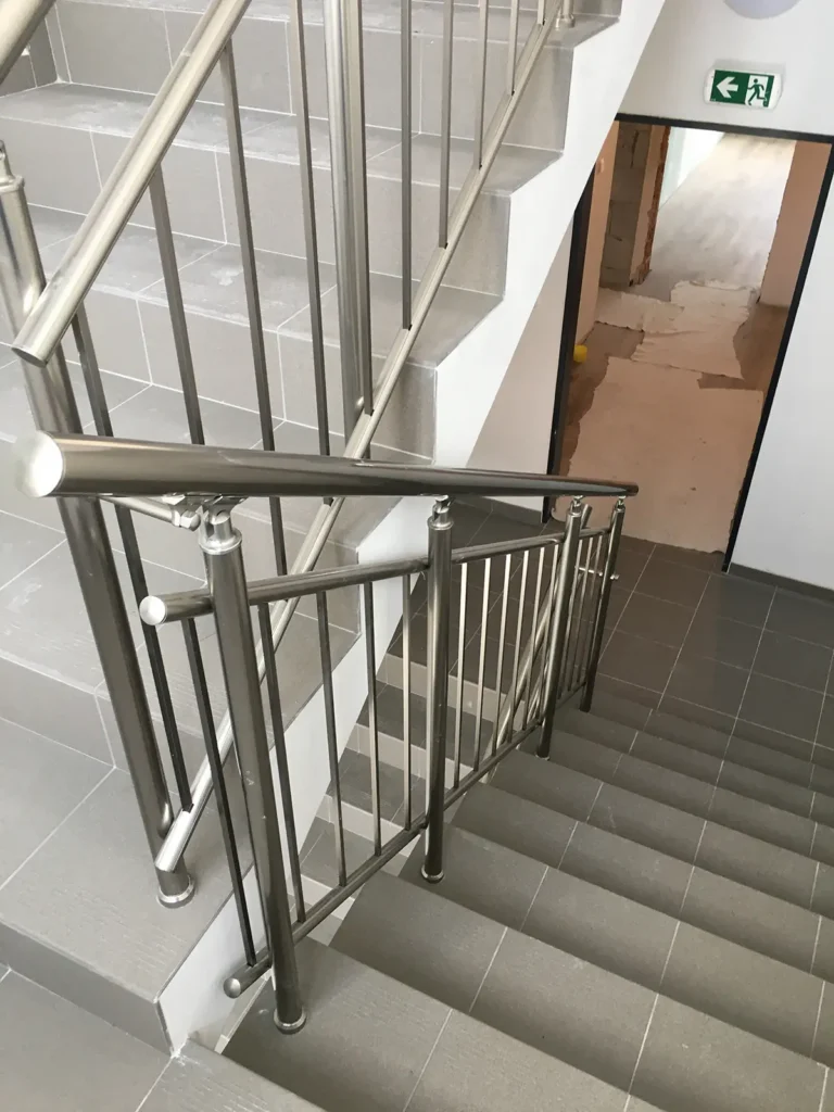 Nerezové zábradlí se svislou výplní na schodišti v interiéru.
