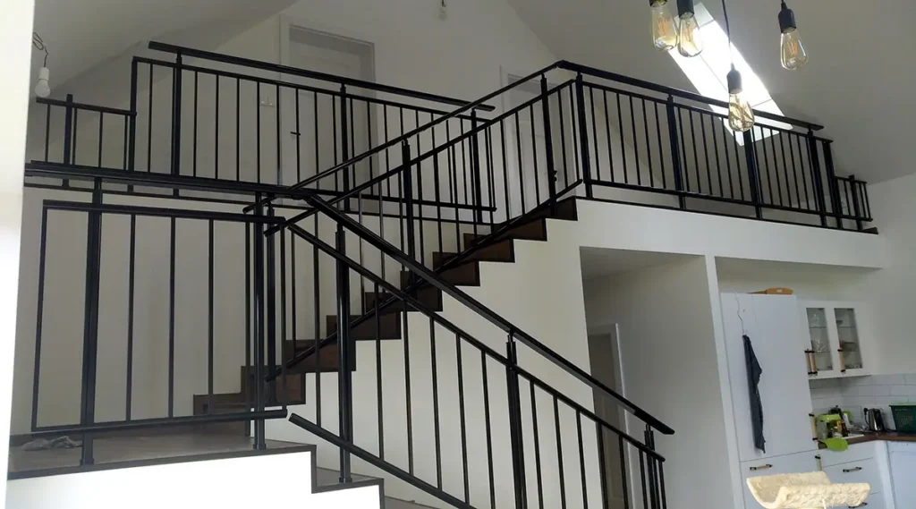 Černé kovové zábradlí se svislou výplní na interiérovém schodišti a galerii.