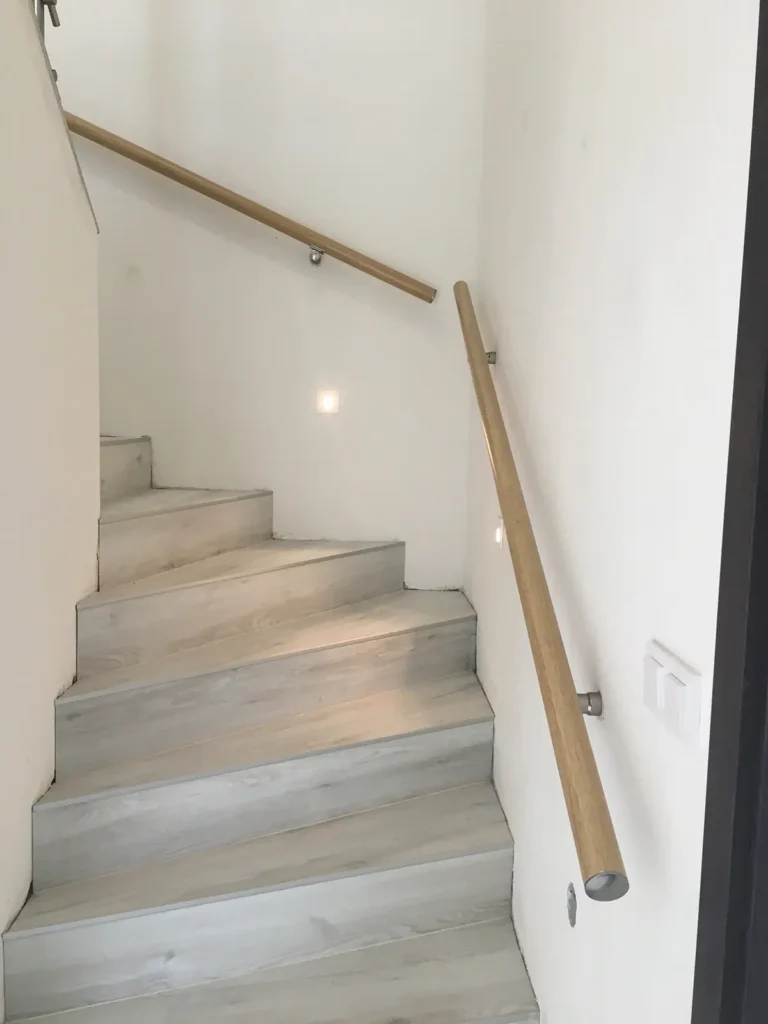 Dřevěné madlo na zeď s nerezovými úchyty podél vnitřního schodiště.