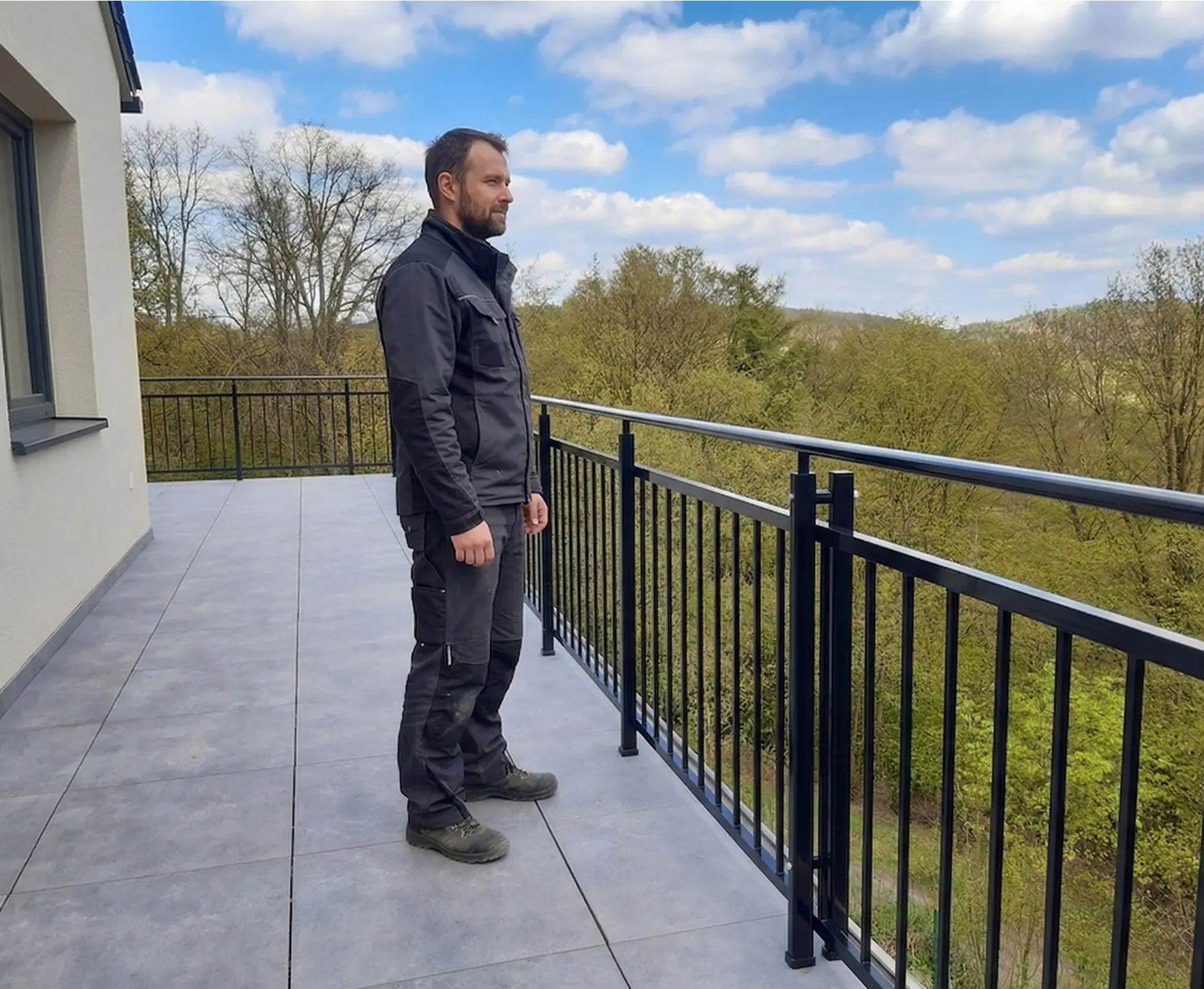 Cerne hlinikove zabradli s tycovou vyplni na moderni terase s vyhledem do lesa.