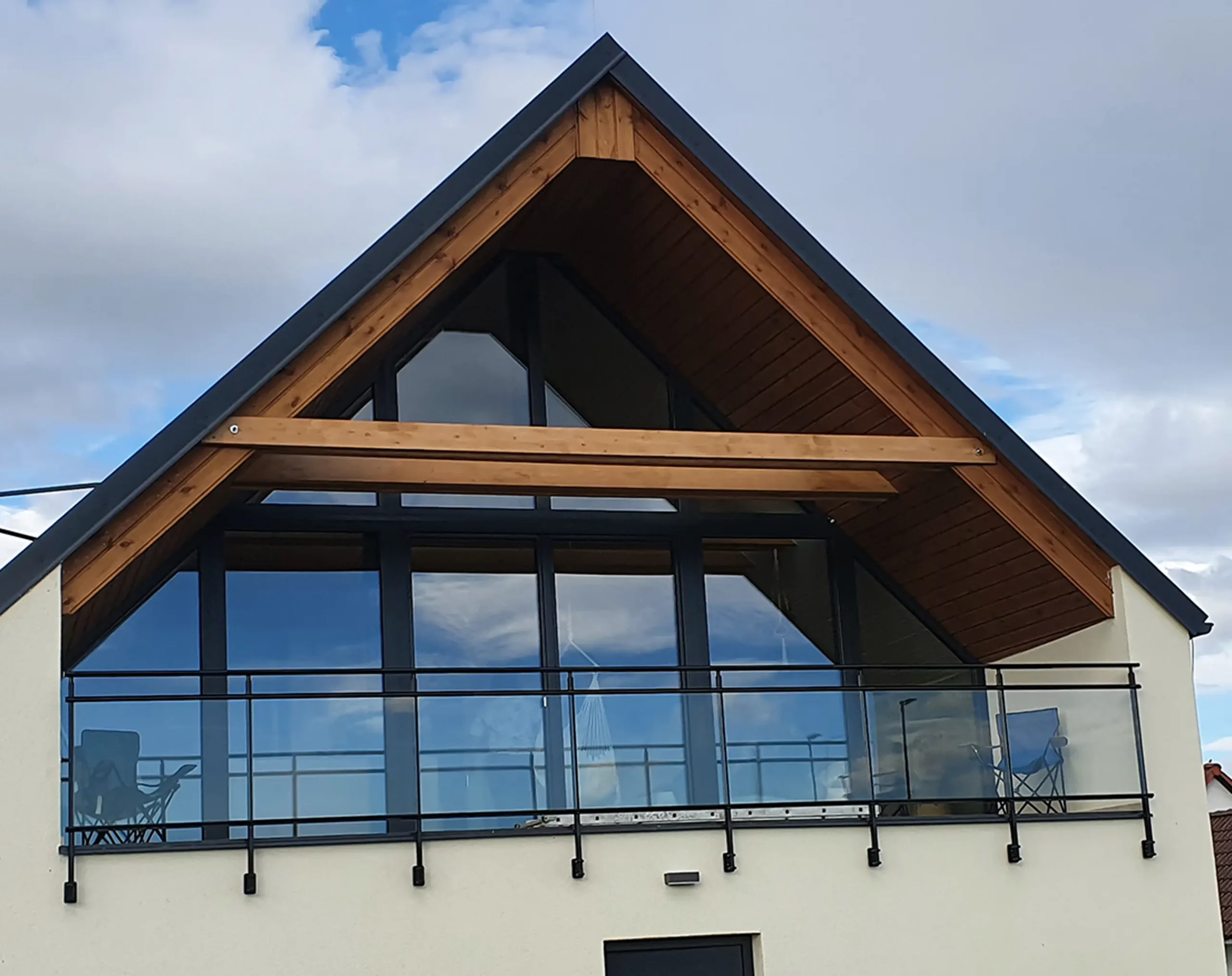 Černé skleněné zábradlí na balkóně moderního domu s dřevěným podhledem.