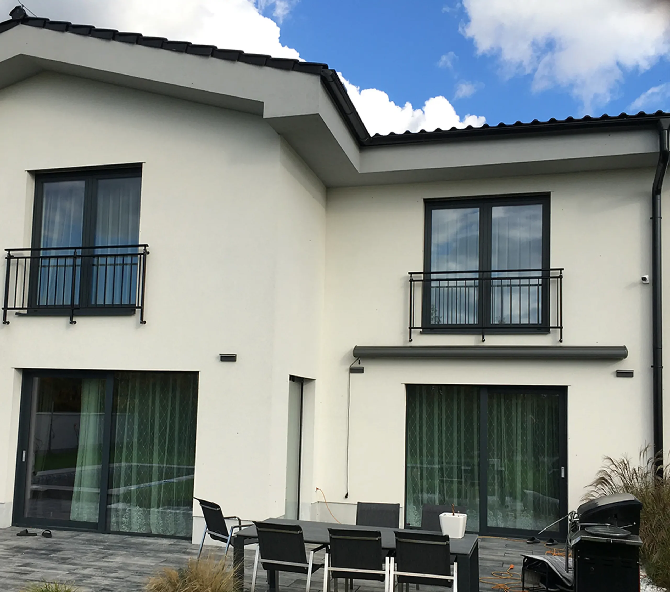 Francouzská okna s tmavým kovovým zábradlím na patře rodinného domu.