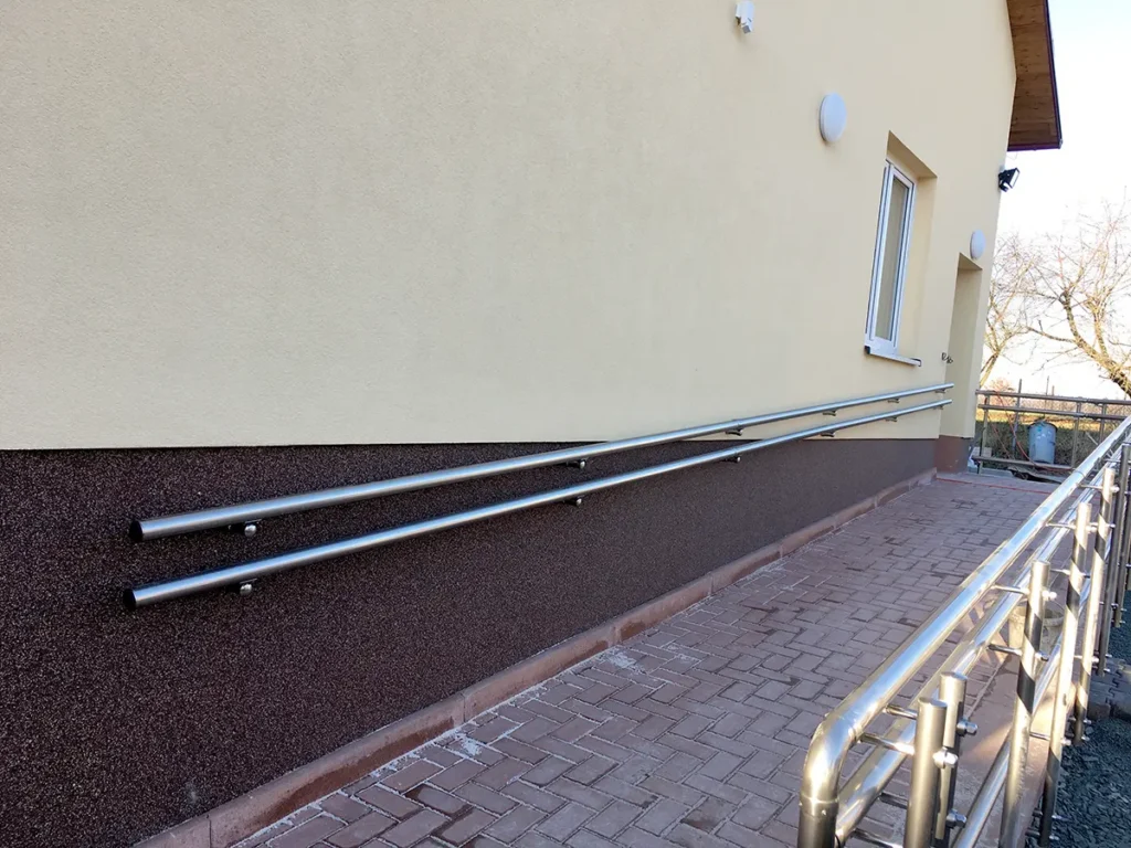 Nerezové dvojité madlo na zeď upevněné na fasádě budovy podél přístupové cesty.