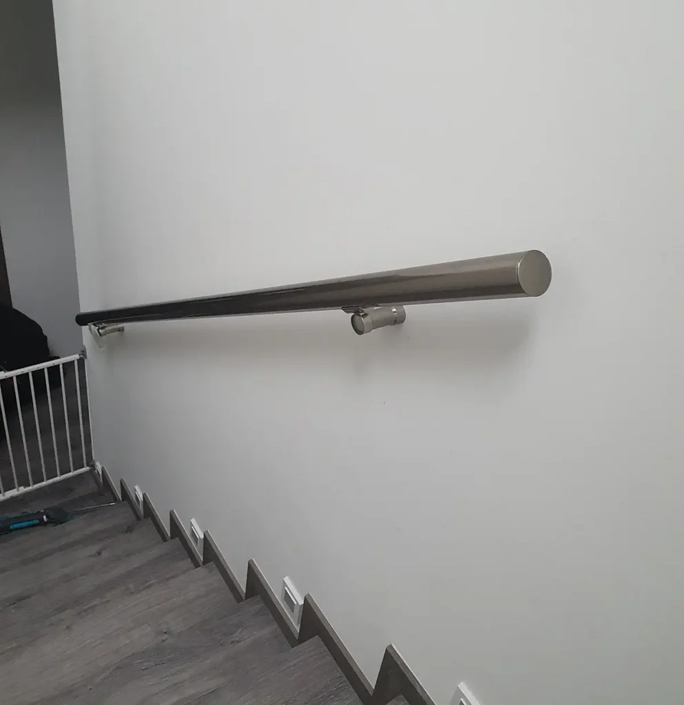 Kulaté nerezové madlo na zeď instalované podél schodiště v moderním interiéru.