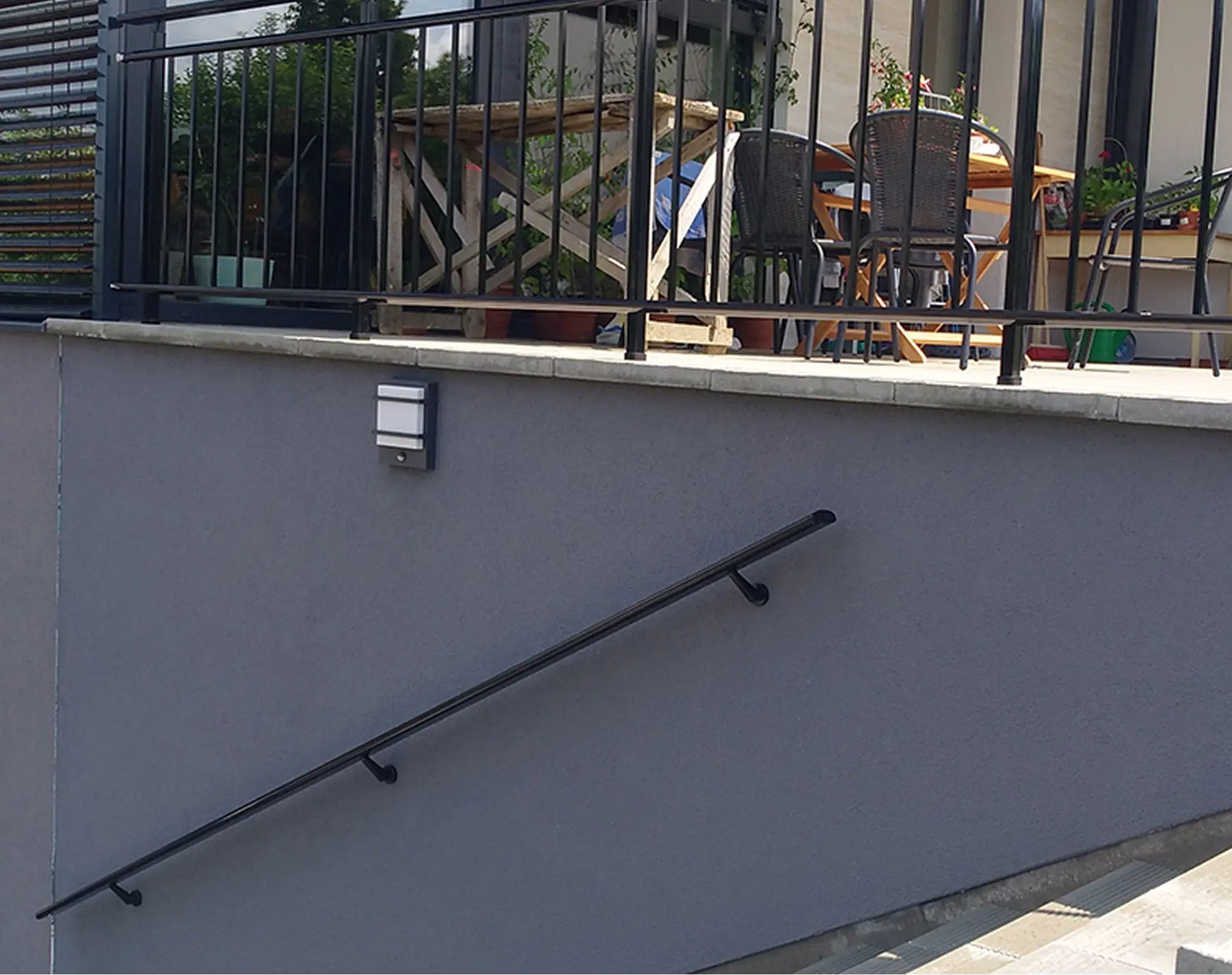 Černé přídavné madlo na stěnu u venkovního schodiště rodinného domu.