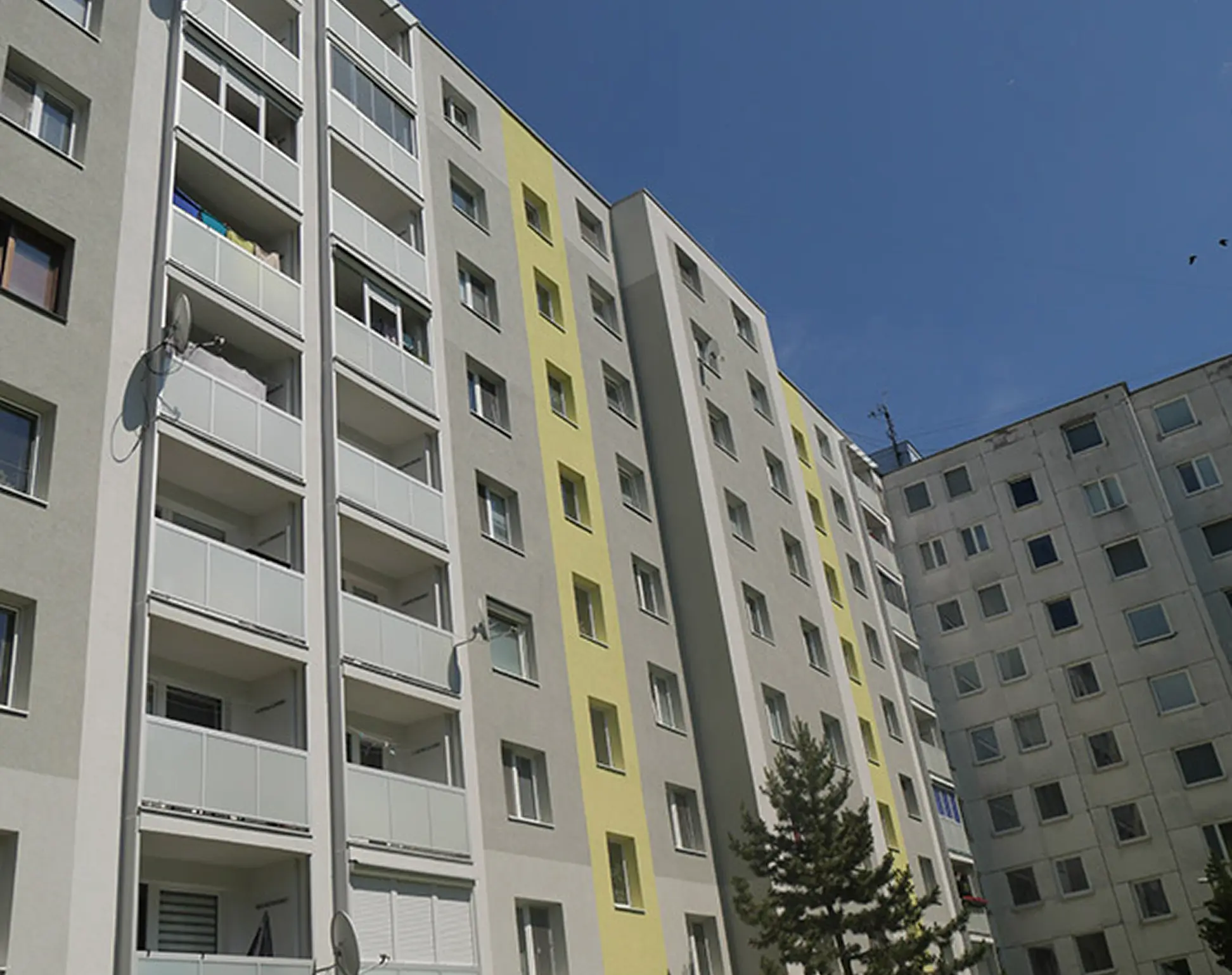 Hliníkové zábradlí pro bytové domy s bílou výplní na rekonstruovaném panelovém domě.