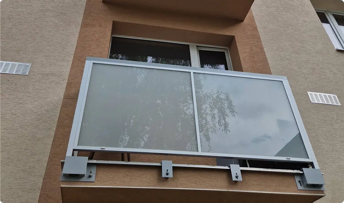 Hliníkové zábradlí s mléčným sklem na balkoně bytového domu.