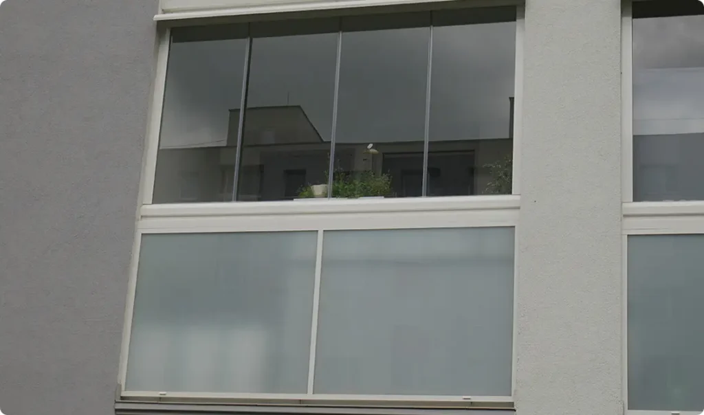 Hliníkové zábradlí pro bytové domy s mléčnou skleněnou výplní a zasklením lodžie.